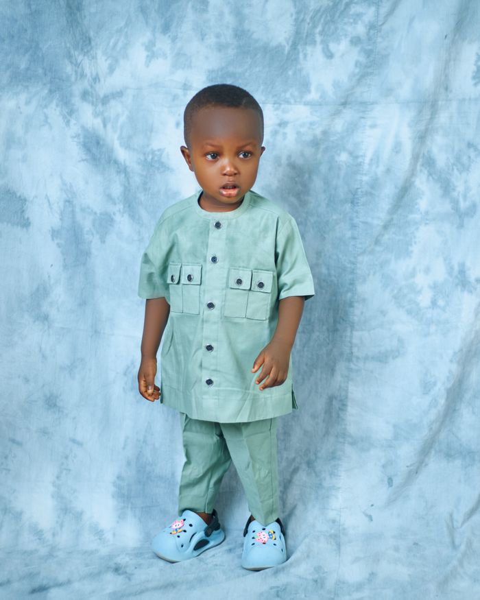 Cute child in a stylish green traditional outfit against a soft blue background.